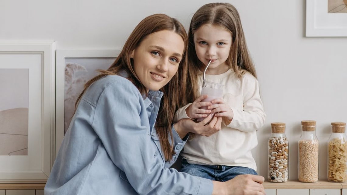 A loving mother with her daughter drinking a smoothie and sharing a warm moment in the kitchen.